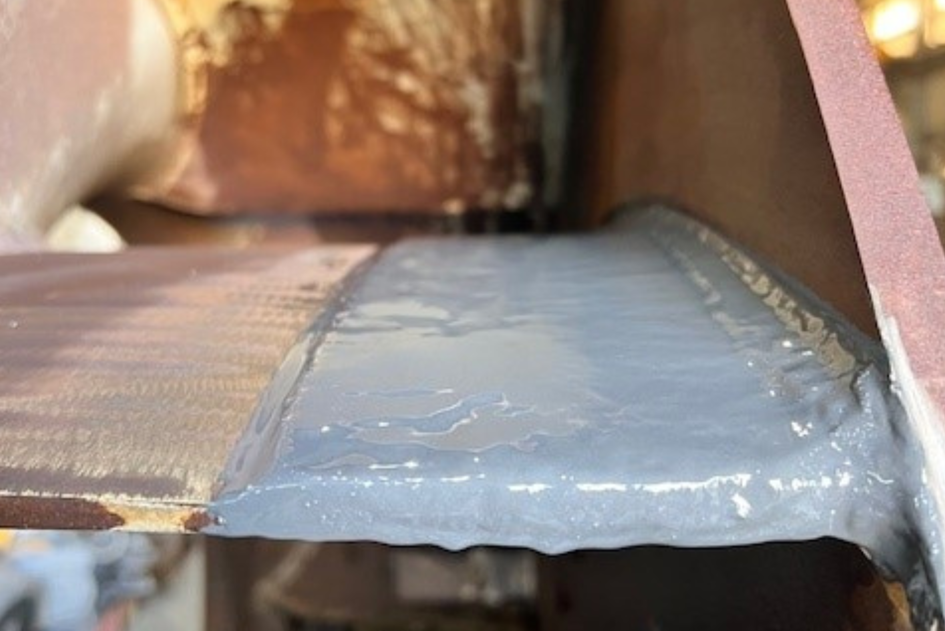 Close-up of a brownish metal structure with a smooth, grey protective coating or sealant applied evenly over the joint.