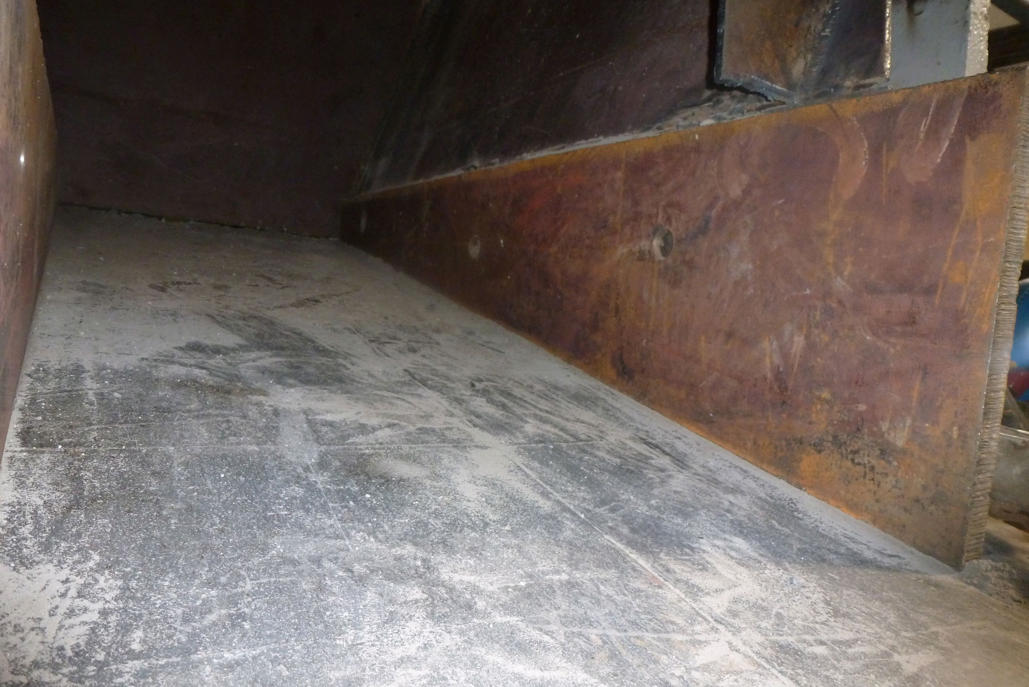 Interior perspective of an industrial steel chute showing a flat base plate alongside a rusted vertical steel side wall plate.