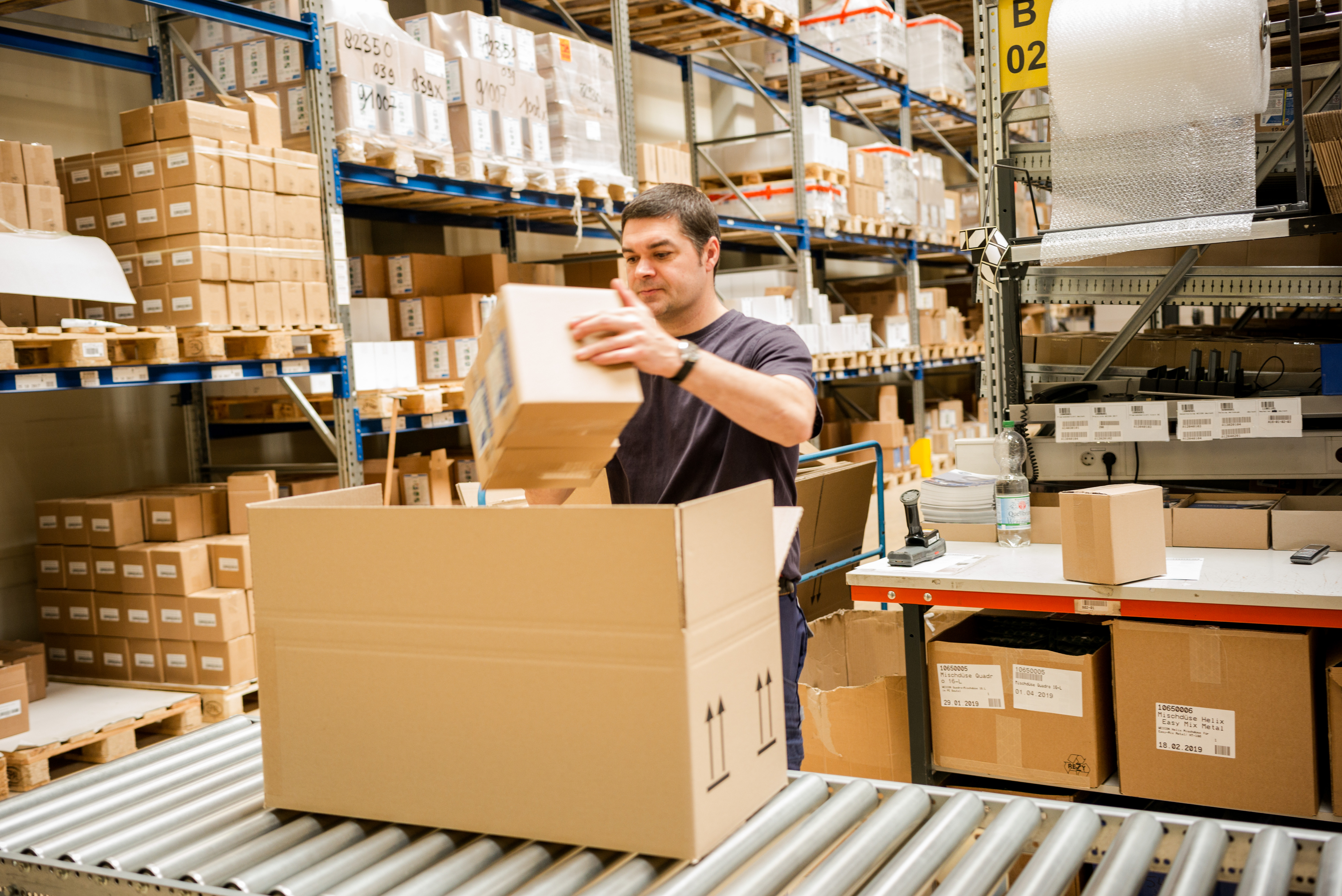 A man standing in a large warehouse and placing a package on a conveyor belt